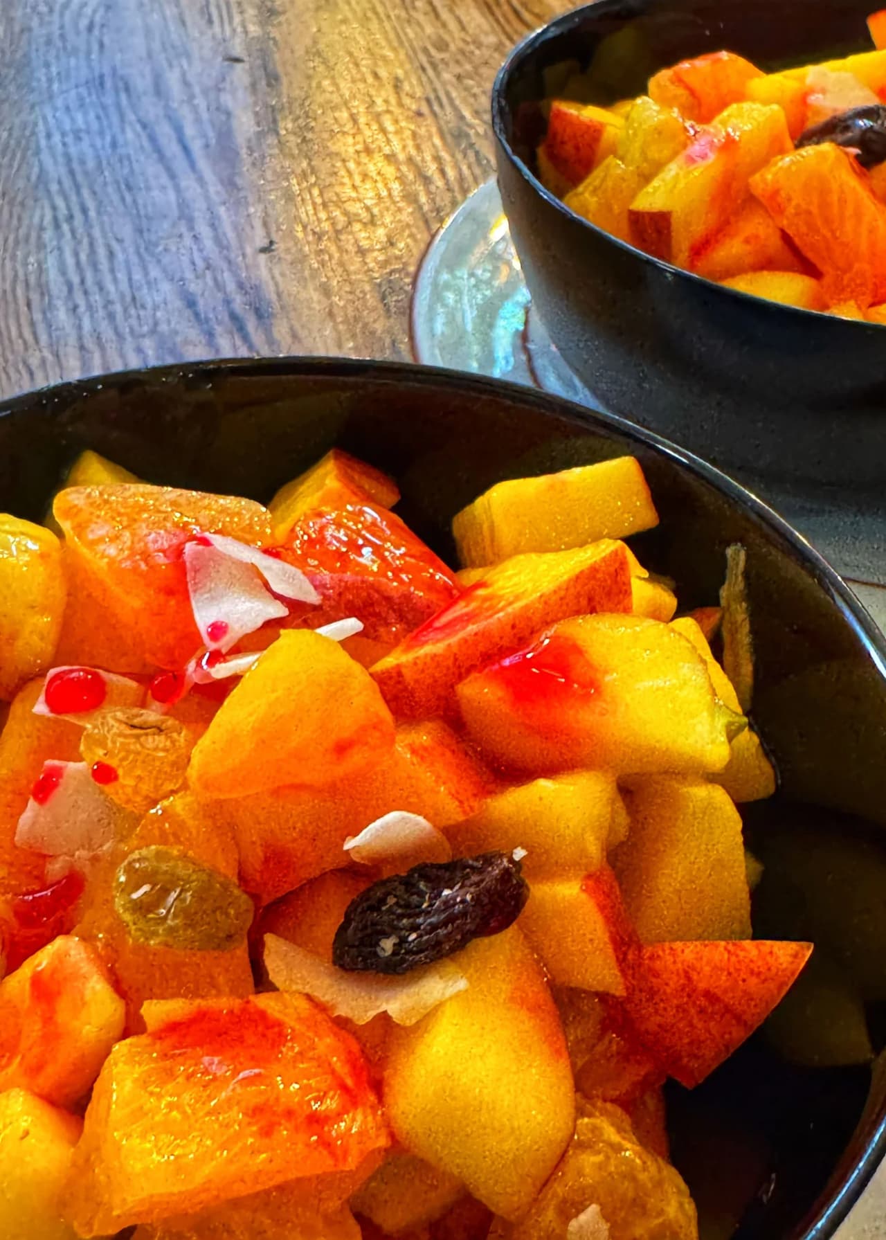 Deux bols noirs contenant une salade de fruits frais avec morceaux de papaye orange, ananas jaune, raisins et fruits confits, servis sur une table en bois au restaurant India Gate