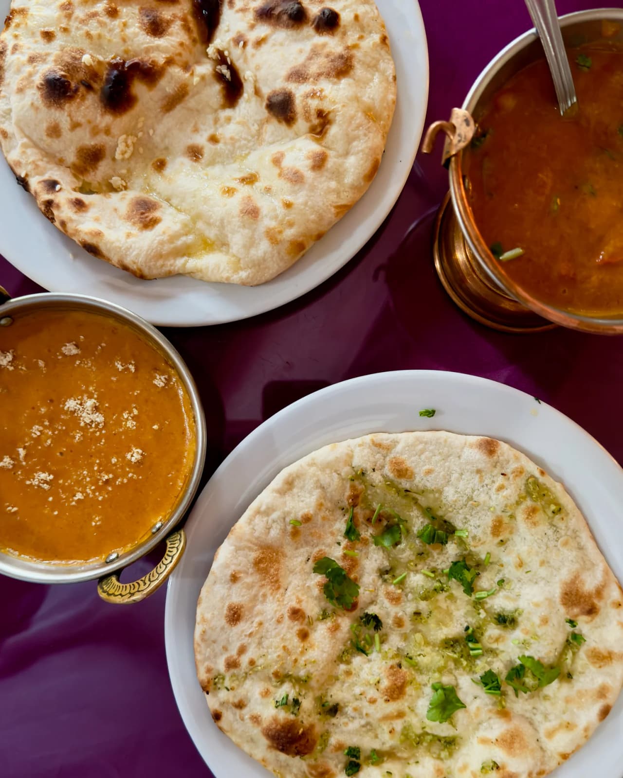 Vue de dessus de plats indiens au restaurant Safran : deux naans dorés sur assiettes blanches accompagnés de bols de curry en sauce dorée et brune, servis sur nappe violette